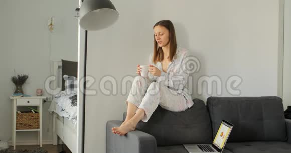 女孩在沙发上喝咖啡或茶女人在房间里工作学习和使用笔记本电脑自由职业写作视频的预览图