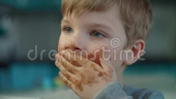 金发男孩在蓝色厨房里吃着脏脸和脏手的巧克力快乐的孩子享受牛奶的肖像视频的预览图