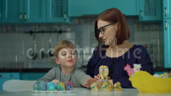 30多岁的母亲和儿子在蓝色厨房的家里吃复活节巧克力兔子快乐的家庭庆祝复活节视频的预览图