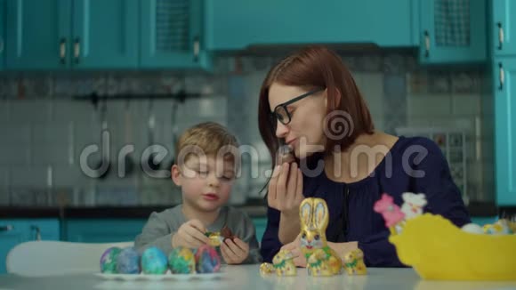 30多岁的母亲和儿子在蓝色厨房的家里吃复活节巧克力兔子快乐的家庭庆祝复活节视频的预览图