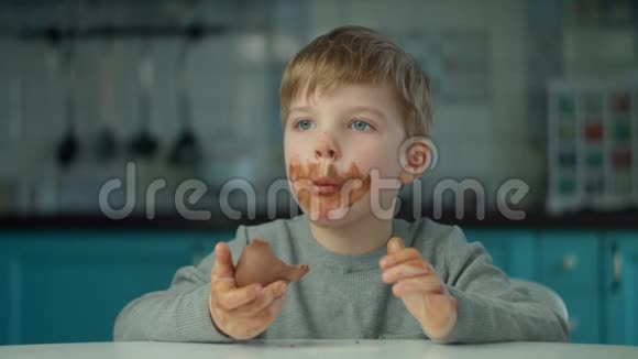 金发男孩在蓝色厨房的家里吃复活节巧克力兔子脸很脏快乐的孩子庆祝复活节视频的预览图