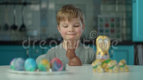 金发男孩在蓝色厨房的家里吃复活节巧克力兔子脸很脏快乐的孩子庆祝复活节视频的预览图