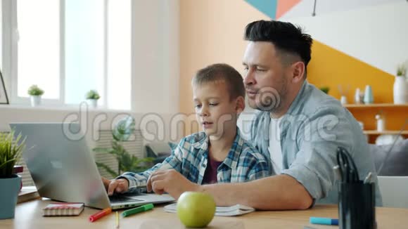 小男孩用笔记本电脑在线学习而父亲则在家里帮助坐在桌子旁视频的预览图