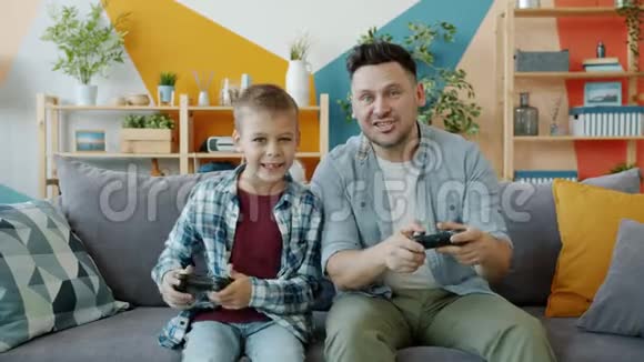 父亲和孩子在家玩电子游戏的肖像按操纵杆上的按钮说话视频的预览图