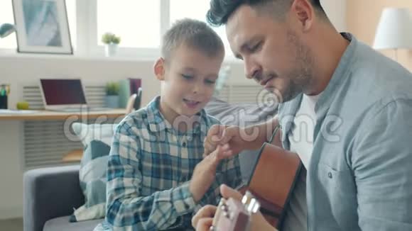 快乐的孩子一边玩吉他一边照顾爸爸创造性的人教他演奏音乐视频的预览图