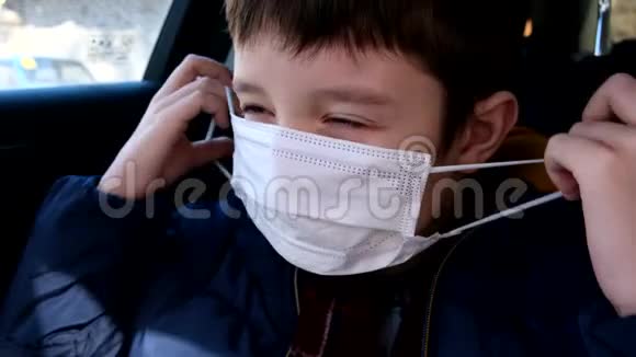 一个十几岁的小男孩在车上戴上白色的保护性手术面罩以防止病毒疾病冠状病毒前视频的预览图