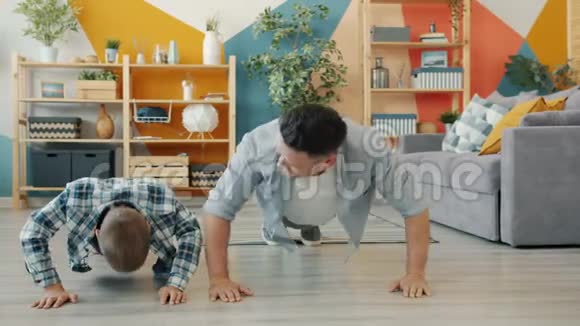 活跃的年轻人和小男孩做俯卧撑然后在公寓里做高五视频的预览图