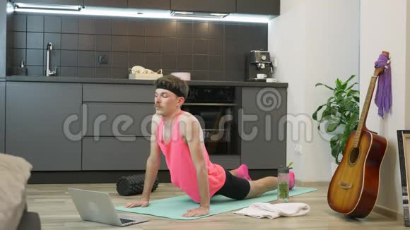 男人在厨房的家中在健身垫上做伸展运动粉色上衣练习伸展和瑜伽练习的搞笑男视频的预览图