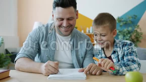 快乐的爸爸为快乐的孩子画有趣的图画在家里的办公桌上玩视频的预览图