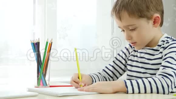 一个学龄前的男孩用彩色铅笔画画坐在桌子旁坐在窗边体贴聪明视频的预览图