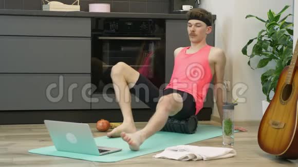 年轻的健身男子与健身卷做康复锻炼使用在线培训应用程序笔记本在家里厨房做运动的人视频的预览图