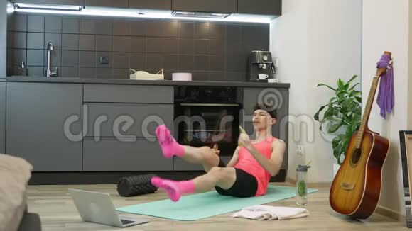 男人在健身垫上做有氧运动使用笔记本电脑上的在线训练应用程序从80年代起穿粉色衣服的搞笑男视频的预览图