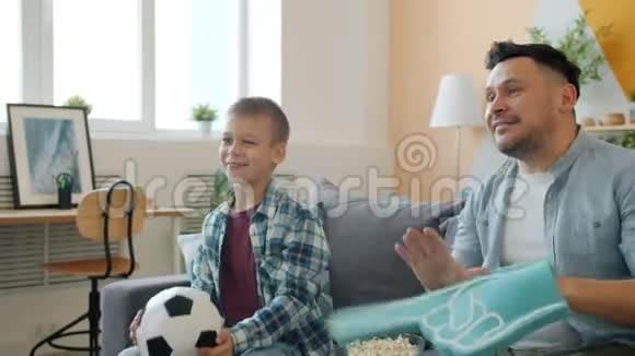 爸爸和儿子在电视上看足球庆祝胜利在家玩球视频的预览图