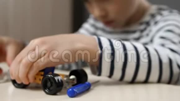 一个小男孩从一个金属建筑套件中建造一个汽车模型扭曲零件车轮螺母螺丝孩子的手视频的预览图
