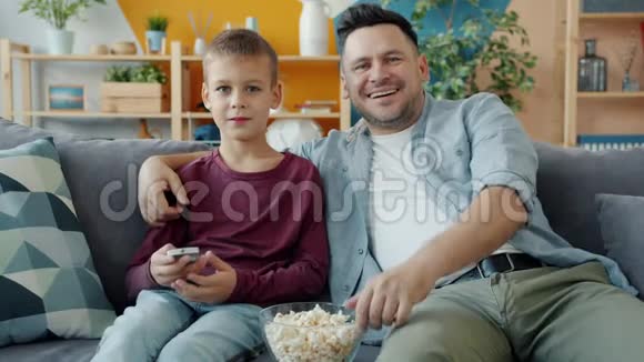 爸爸和儿子坐在沙发上一起欣赏滑稽电影的慢动作视频的预览图