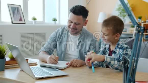 父亲和儿子正拿着笔记本电脑坐在办公桌前笑着说话视频的预览图