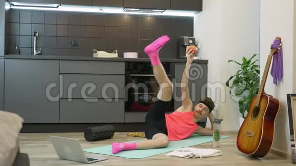 男人在家做健身和有氧运动在厨房使用在线培训应用程序在笔记本电脑上粉色运动的搞笑男视频的预览图