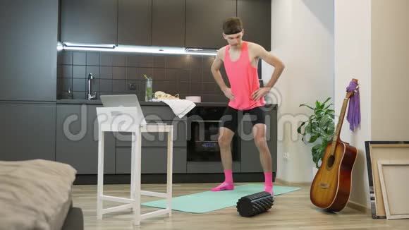 有趣的健身者带着胡子和粉红色的衣服在笔记本电脑上观看在线有氧课在电脑上做健身运动视频的预览图