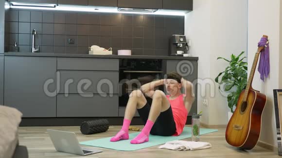 健身男在家厨房做腹部运动使用笔记本电脑上的在线培训应用程序粉红色的年轻滑稽男子视频的预览图