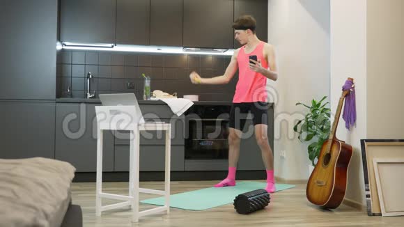 多任务运动健身穿着粉色上衣的有趣性感男人在肱二头肌上做锻炼在网上看健身课视频的预览图