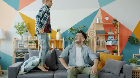 活跃的男孩在沙发上跳玩得开心然后和快乐的爸爸一起做击掌视频的预览图