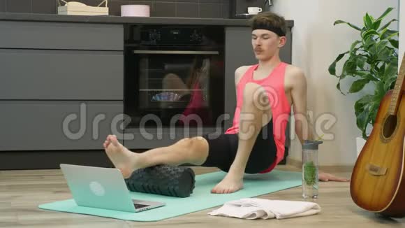 在隔离期间男人在家中厨房用健身卷做按摩有健身卷的年轻人在做康复锻炼视频的预览图