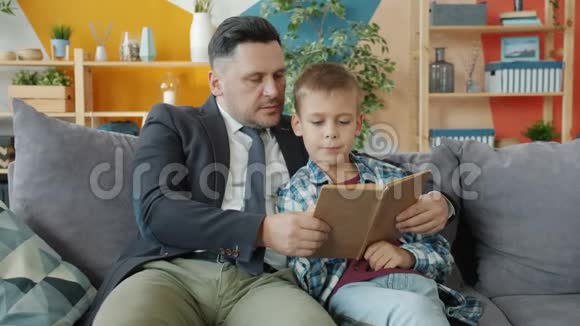 爸爸商人教小儿子在家里坐在沙发上看书视频的预览图