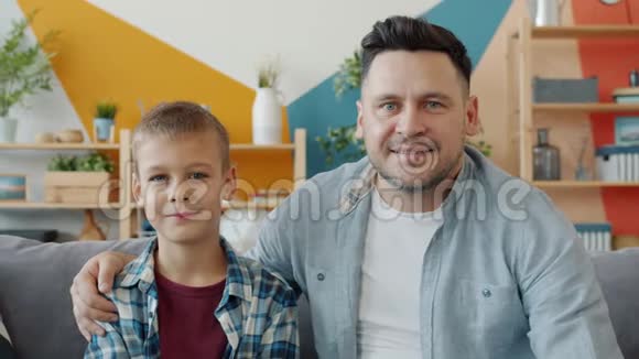 两个人的肖像年轻的成年父亲和可爱的小儿子在家里沙发上微笑视频的预览图