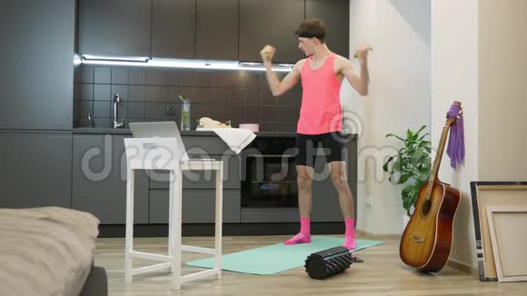 穿着粉色衣服在家里用香蕉在肱二头肌上做锻炼的人真是个滑稽的蠢蛋有代表性的男性运动员观看视频的预览图