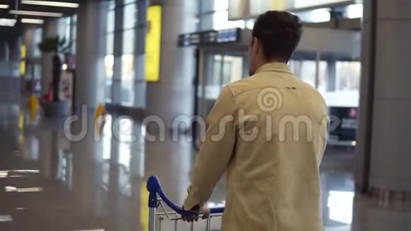 布吕内特一个穿着米色衬衫的留胡子的人带着行李手推车在国际机场散步匆忙中走着视频的预览图