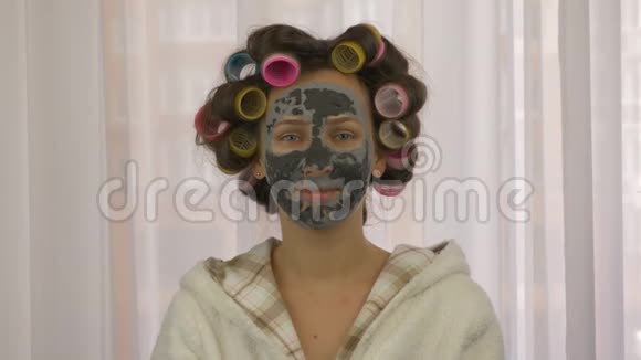 女性肖像头上有卷发脸上有粘土洁面黑色面具特写照顾皮肤复合体的年轻女性视频的预览图