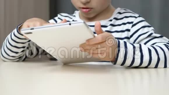 男孩用平板电脑体贴地看着平板电脑屏幕孩子总是坐在桌子旁用视频的预览图