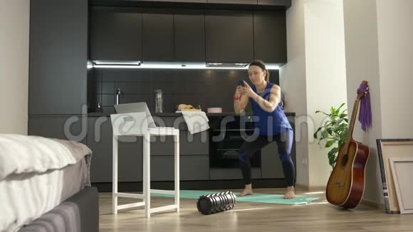 多任务运动健身女人在厨房里用智能手机蹲在家里适合忙于手机工作的女性视频的预览图