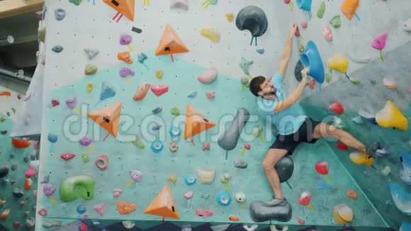 穿着运动服的壮汉在健身房攀爬五颜六色的人造墙抓着石头视频的预览图