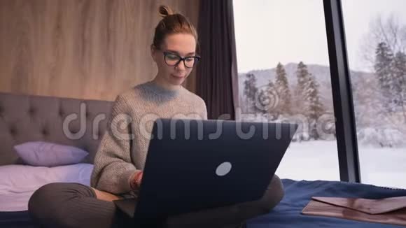 一幅漂亮的自由职业者女孩戴着眼镜的画像床上有一台笔记本电脑在一里后面有透明的墙视频的预览图