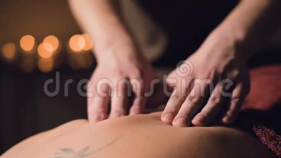 年轻的男性按摩治疗师正在按摩房间里的一个纹身的女人的背部做手指按摩的灯光视频的预览图