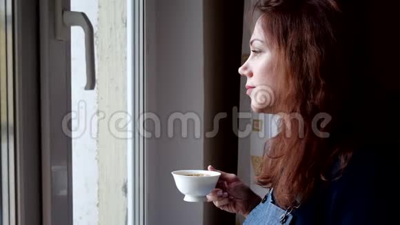 在隔离期间年轻女子喝着咖啡看着窗外社会距离视频的预览图