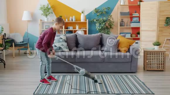 用吸尘器做家务的小男孩在家里用吸尘器吸尘地板的慢动作视频的预览图