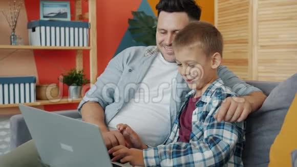 父子俩一起坐在沙发上用笔记本电脑聊天视频的预览图