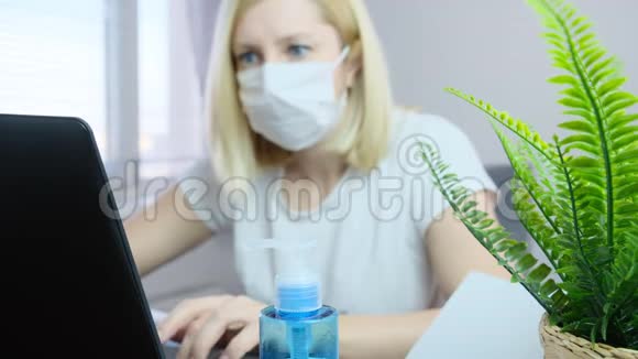 在家工作的笔记本电脑上戴着口罩的模糊的女性自由职业者洗手液作为一种保护物就在前面的桌子上视频的预览图