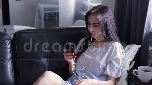 年轻的黑发女人在耳朵里插入耳机看着电话视频的预览图
