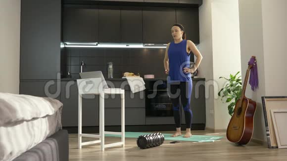 女人在厨房里跳和做健身有氧运动使用笔记本电脑上的在线训练应用程序适合运动的女孩视频的预览图