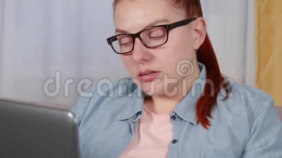 一个疲惫的年轻女人坐在客厅里用笔记本电脑工作的肖像视频的预览图