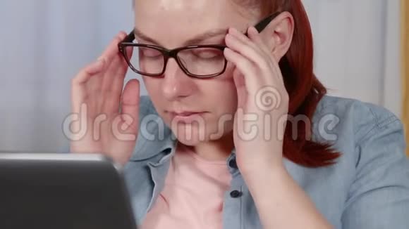 美丽的年轻女子从脸上摘下眼镜以免疲劳在客厅的笔记本电脑上远程工作视频的预览图