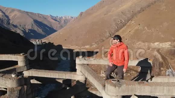 一个男性极端痞子坐在高山高泥流防护结构顶部的空中景观视频的预览图
