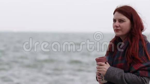 一个留着红色长发的小女孩穿着一件保暖外套和羊毛围巾拿着一个金属热水瓶上面放着一杯热饮料头发视频的预览图