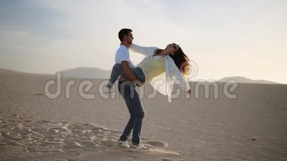 在空旷的沙漠中年轻夫妇的完美场景男人抱着她的女人把她转过来在沙漠里玩得开心视频的预览图