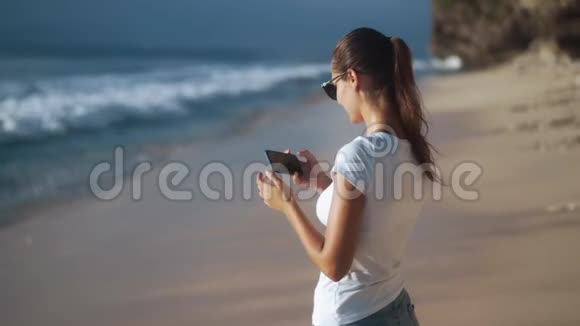 戴太阳镜的年轻漂亮女人在海滩拍照视频的预览图