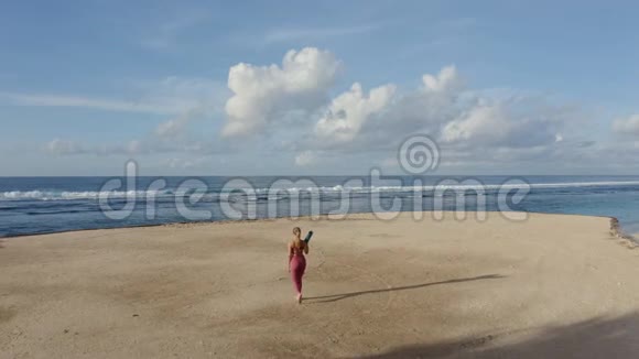 空中景色年轻女子穿着运动服带着体操垫去海滩视频的预览图