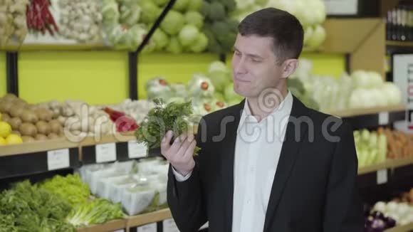 一幅白人男子微笑的肖像闻着杂货店里新鲜的绿色植物穿西装的年轻人选择迪尔视频的预览图